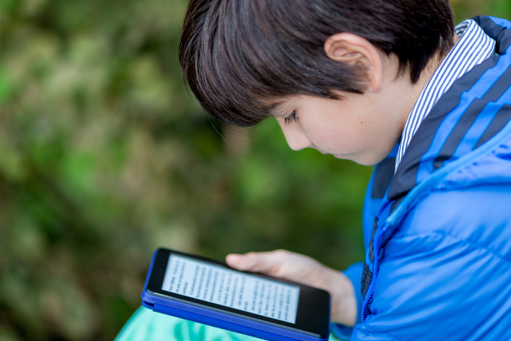 A grade school boy reads a book on a tablet