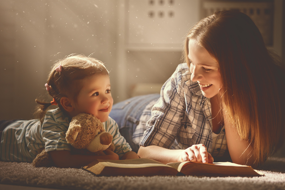 A mom and daughter read a book on the living room floor together