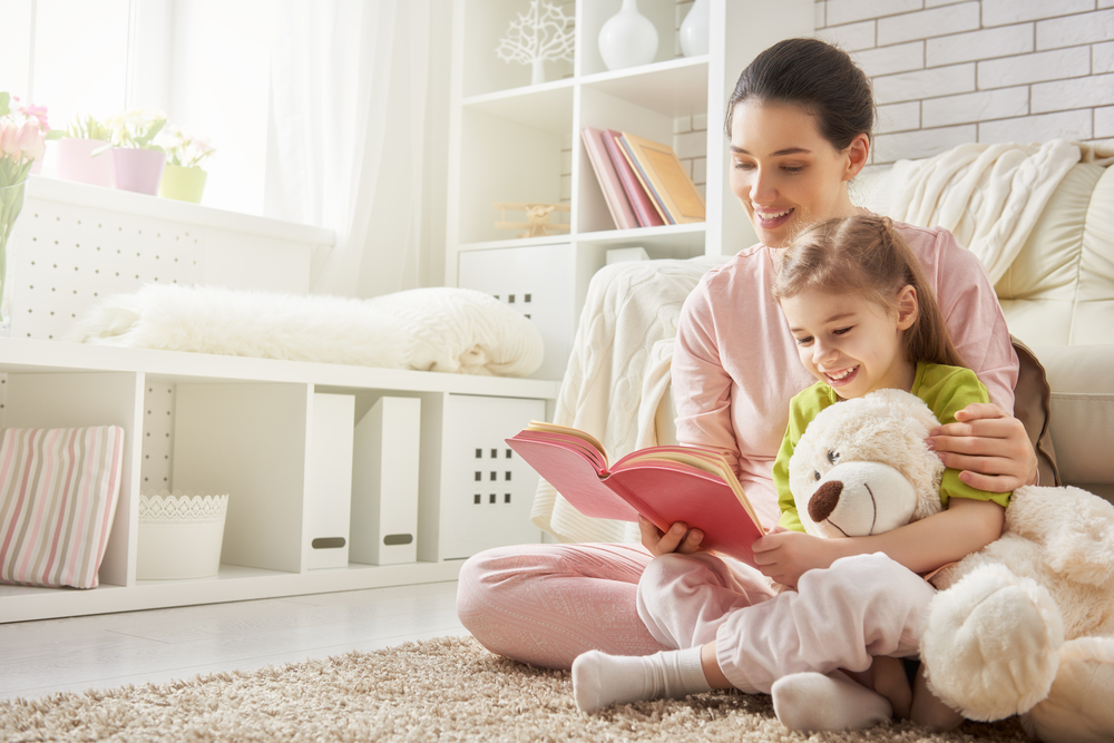 A mom and daughter read a book together on the living room floor