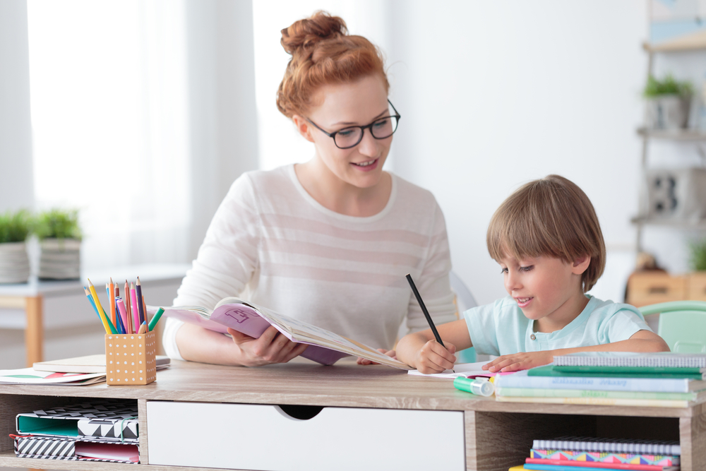 A female tutor helps a young boy with homework