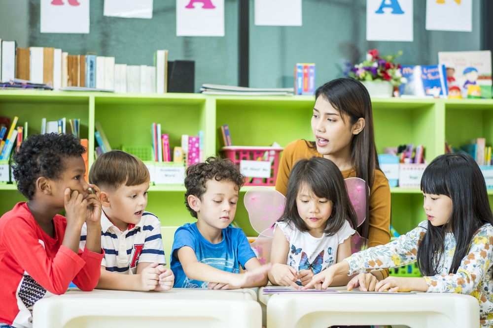 Teacher assisting a kindergartener with a phonics reading app to help with literacy.