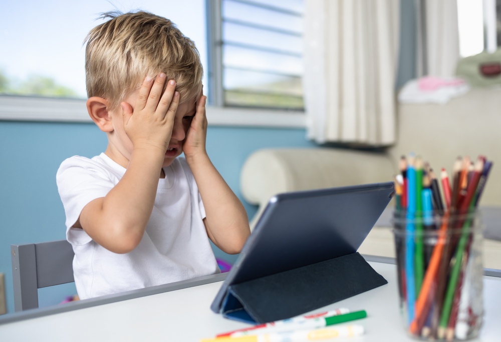 Young boy frustrated while trying to read on a digital tablet, representing children struggling to read.