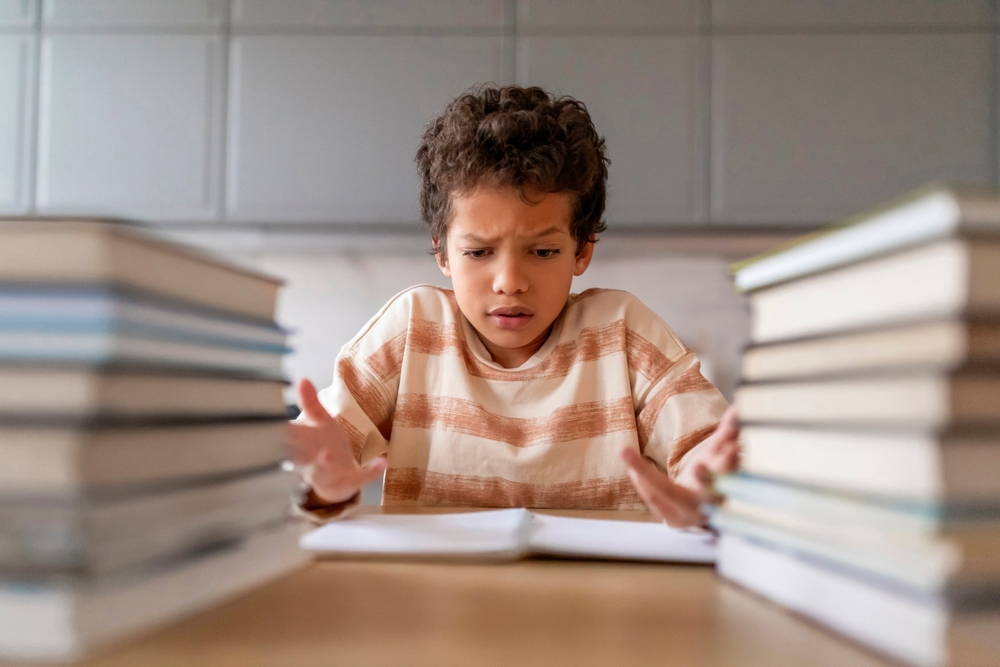 Child struggling with reading comprehension surrounded by books, indicative of common causes of poor reading comprehension in students.