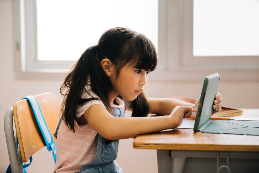 Young girl using a science of reading app for kids on her tablet at home, demonstrating interactive literacy development