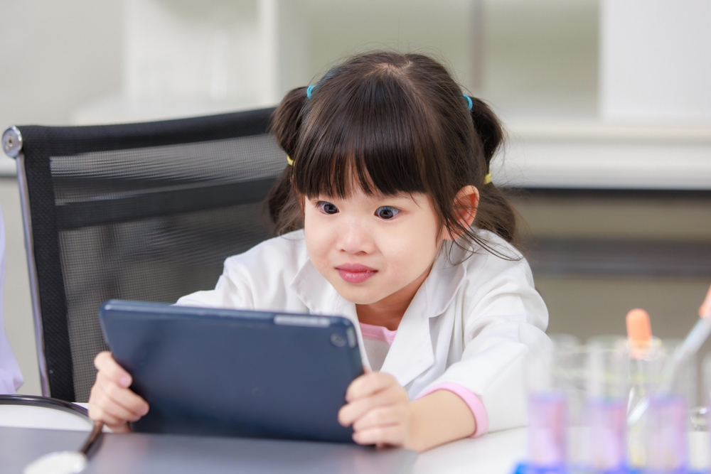 Young girl using a learn-to-read app for kids on a tablet in a classroom
