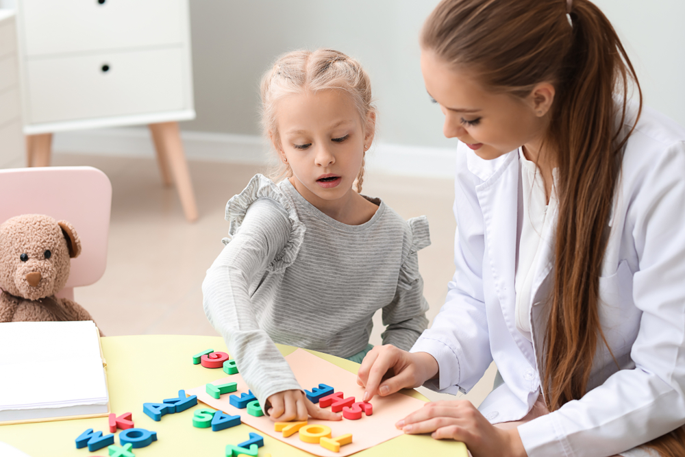 Educator helping dyslexic child with reading using letters